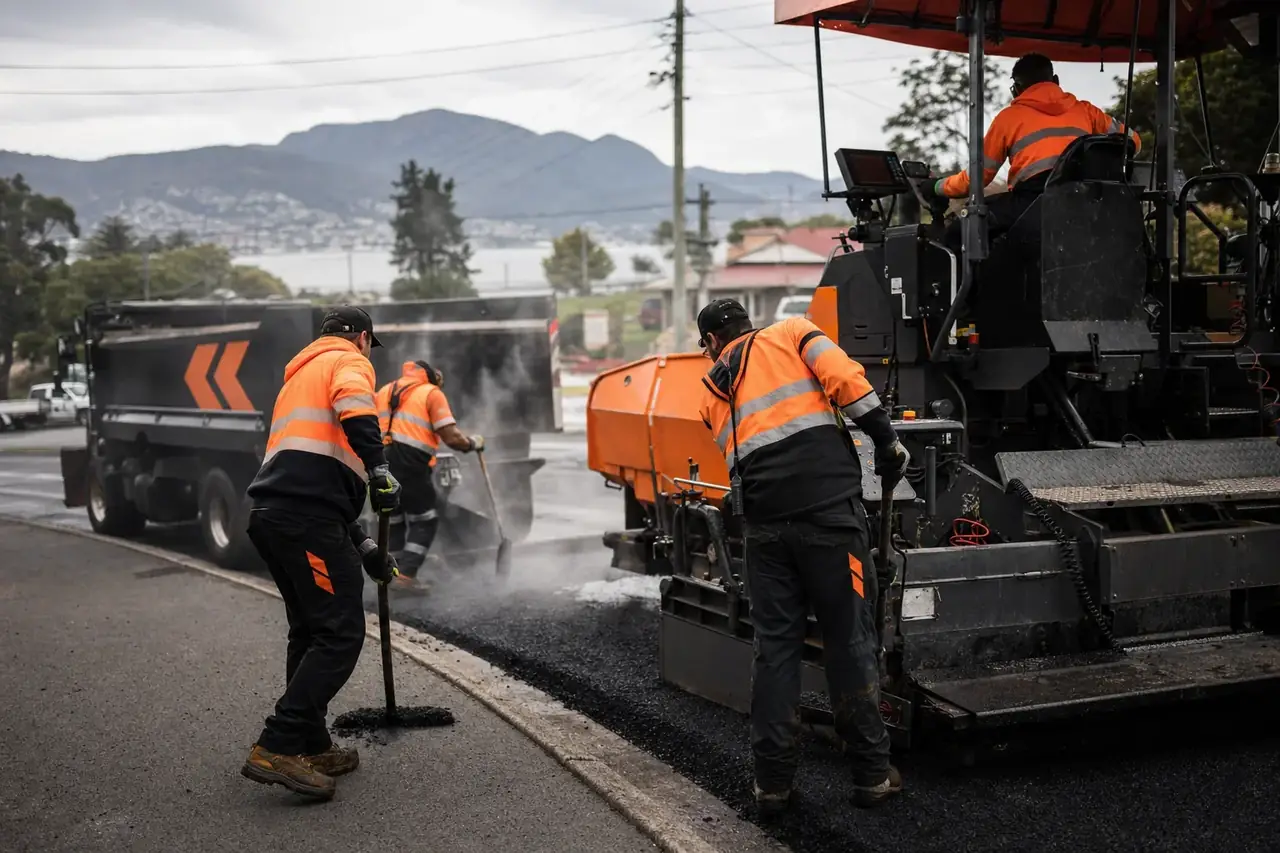 Asphalt paver and hi-vis crew laying hot mix on a Hobart street with kunanyi in the background